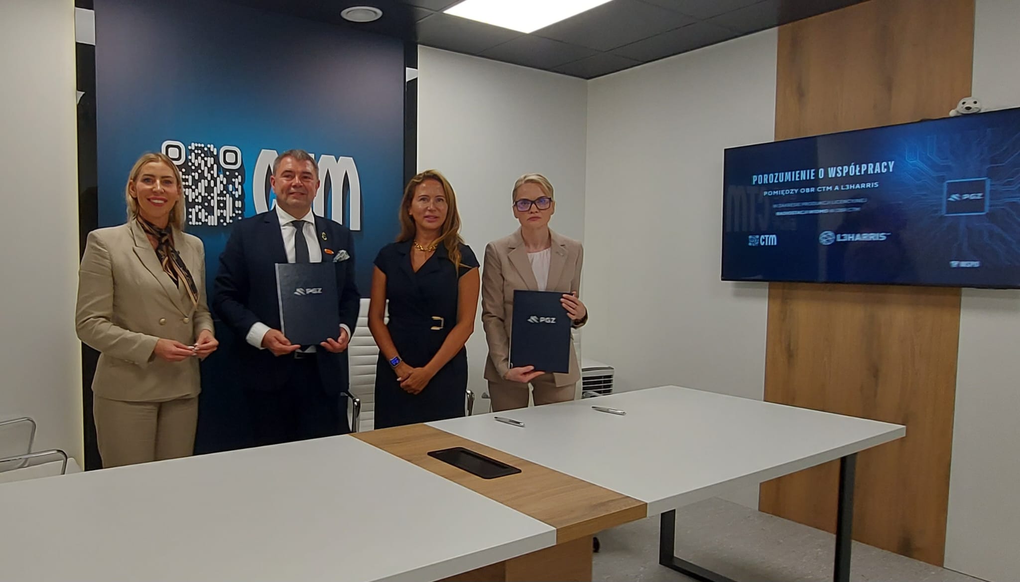 Zdjęcie grupowe po podpisaniu porozumienia OBR CTM i L3Harris — przedstawiciele firm z teczkami PGZ, w tle ekran z tytułem porozumienia